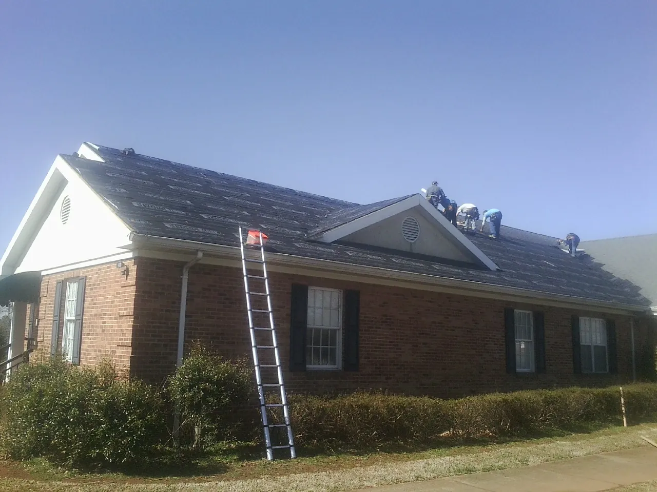 Crew tearing shingles off a brick ranch roof with a ladder set — Metal Roof Repair work by our crew in Moorefield