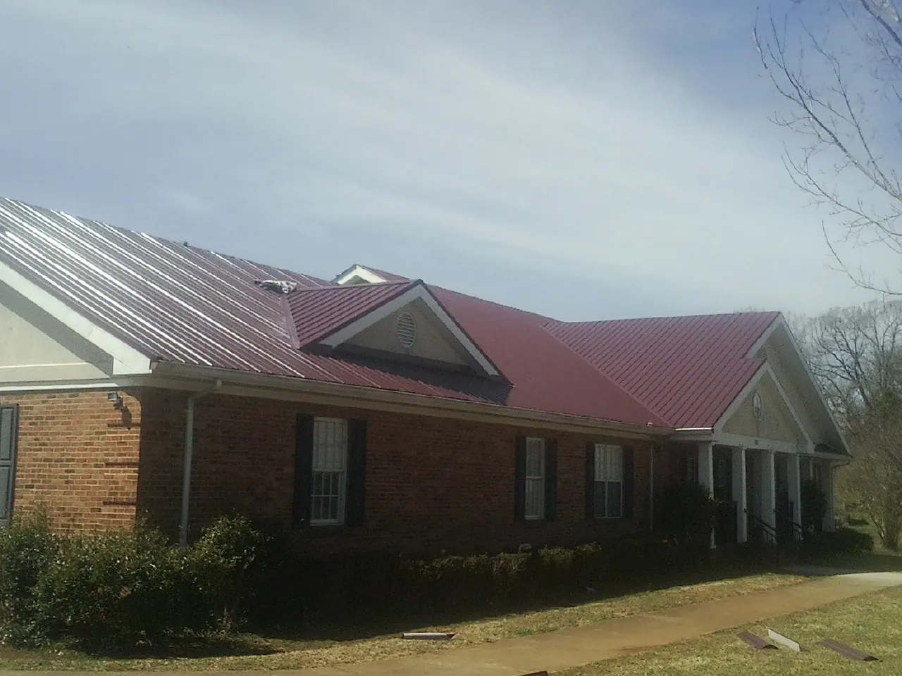Red metal roof with gabled entries on a long brick building, from a Hail Damage Roof Repair job in Moorefield