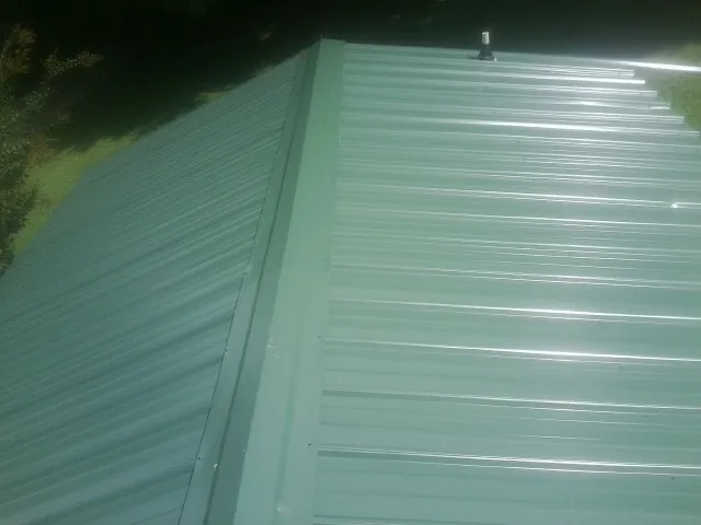New green metal panels meeting at the ridge of a roof — Flat Roof Repair work by our crew in Moorefield