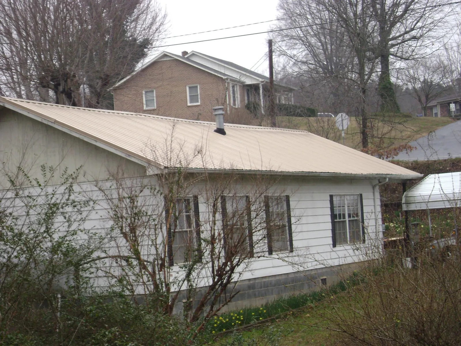 Tan metal roof on a white sided house set into a hillside — Commercial Roofing by Roofing Brothers in Moorefield