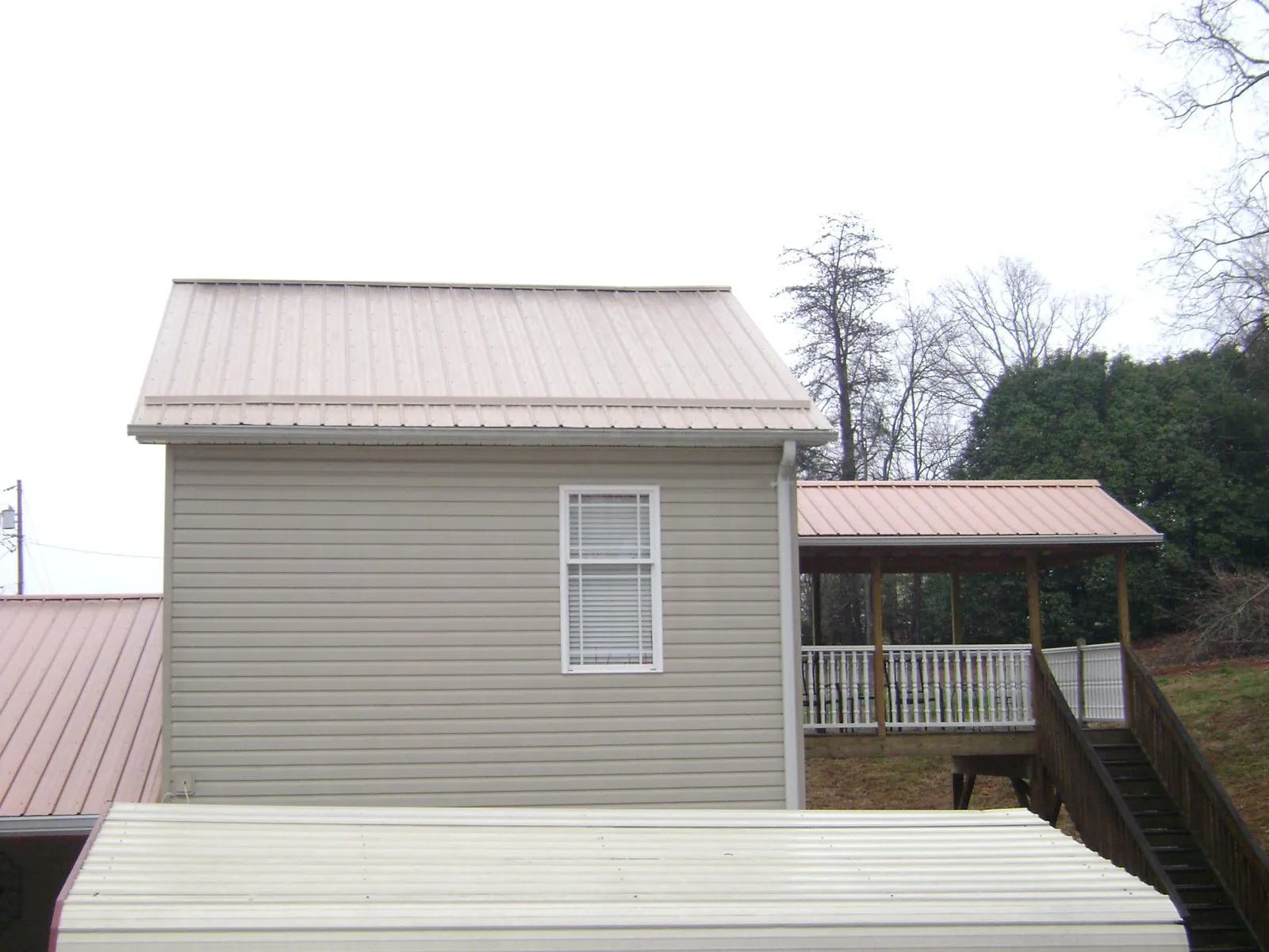 Tan metal roofs on a two story addition and attached porch, from a Roof Replacement job in Moorefield